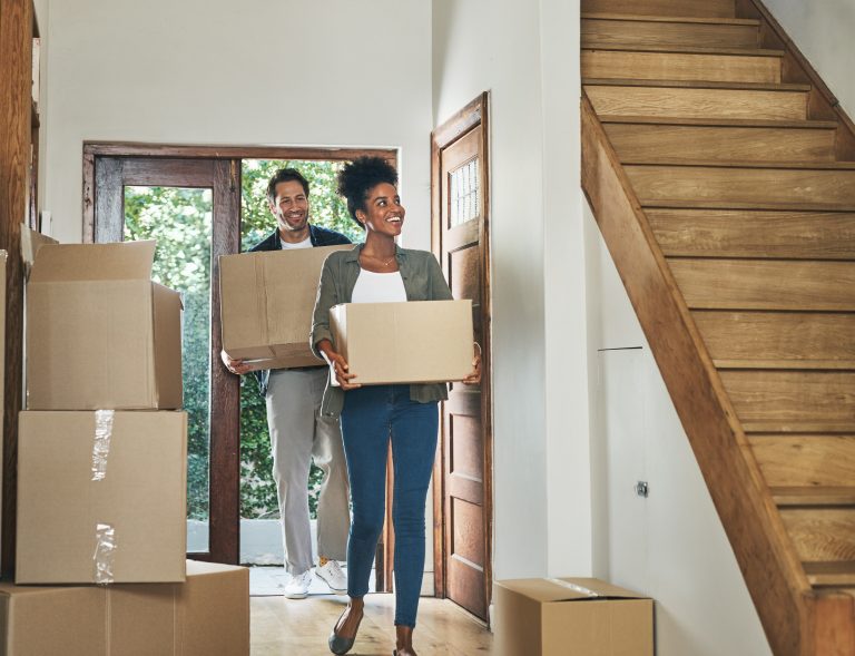 A happy, interracial couple carrying boxes and moving into a new home